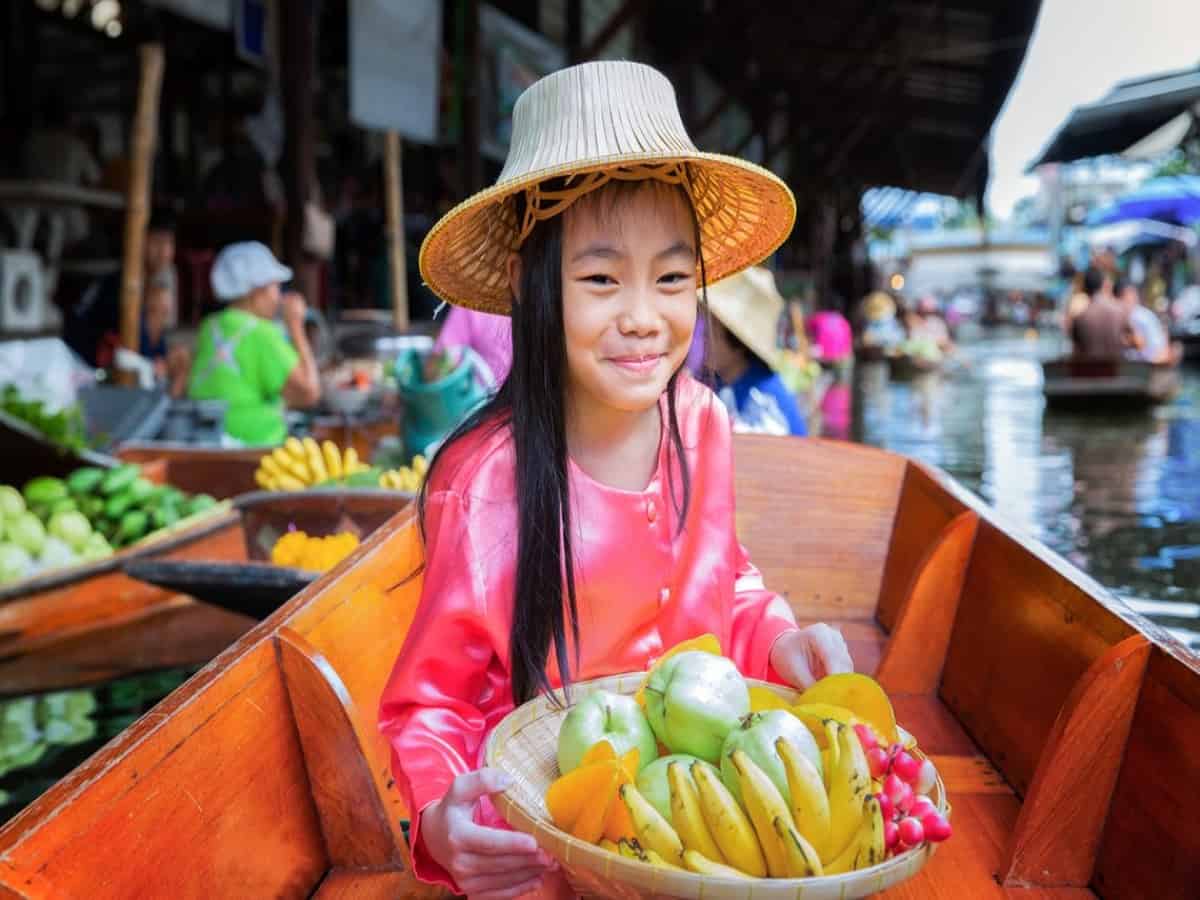chikd sit on the boat and hold the fruit basket in traditional floating market , thailand.