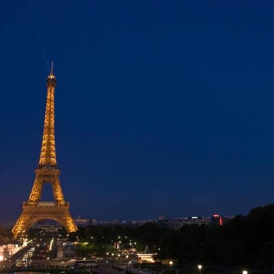 wide shot of the eiffel tower lit up in the evening with the moon in view and the rest of the city of paris