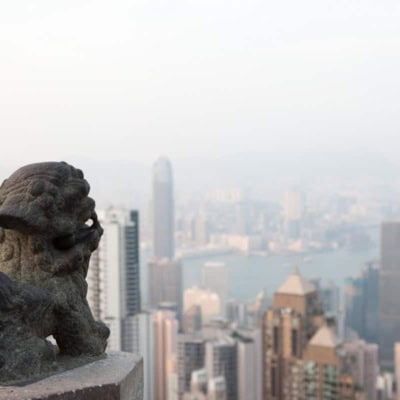 lion statue to the left and the hong kong skyline from victoria peak