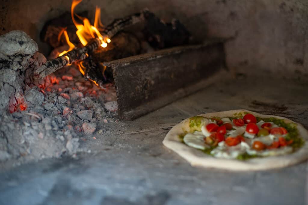 fresh pizza with tomato and mozzarella cooking in a wood fire oven.