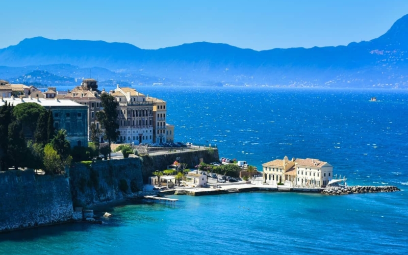 aerial view of buildings on corfu island surrounded by water with mountain range in distance