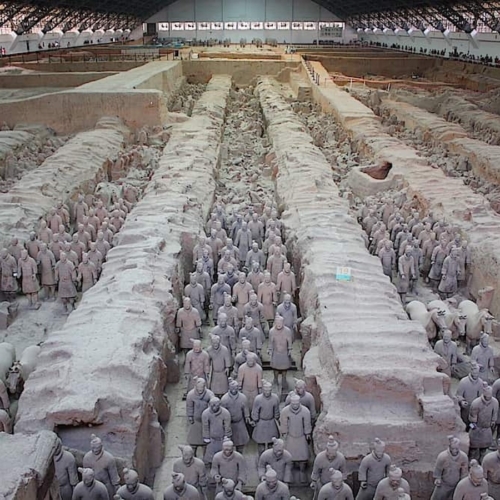Rows of terracotta warrior statues stand in excavated pits inside a large covered archaeological site, part of the Terracotta Army in Xi'an, China.
