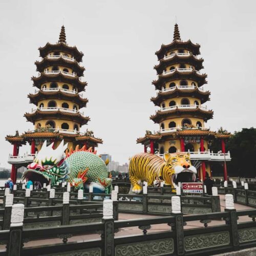 Two traditional Chinese pagodas stand side by side, with large dragon and tiger statues at their entrances, on a cloudy day.