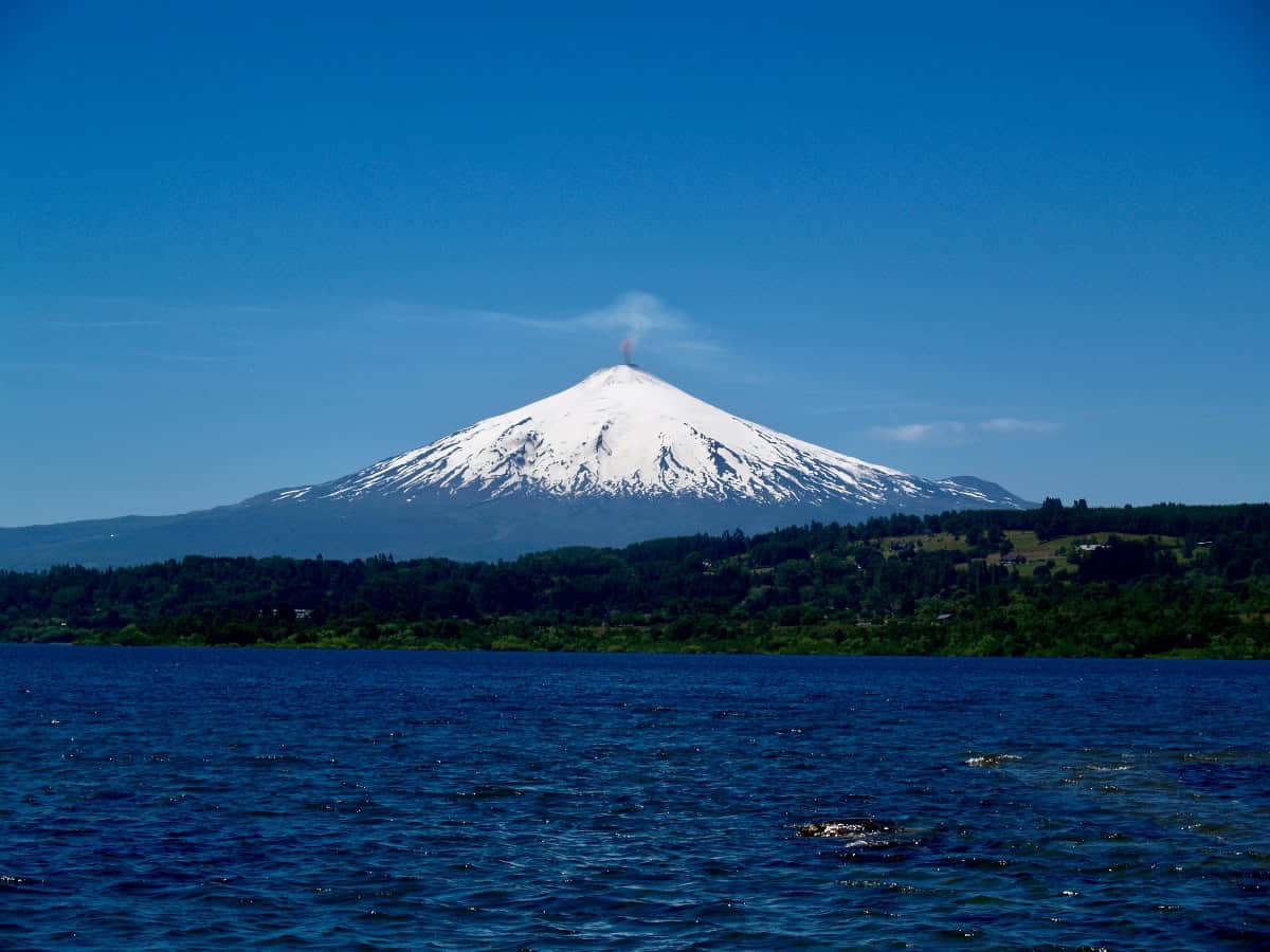 view of villarrica volcano covered in snow from across lake
