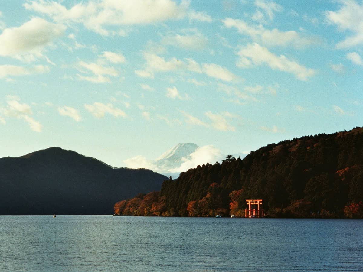 distant view of hakone shrine across water in front of mt. fuji