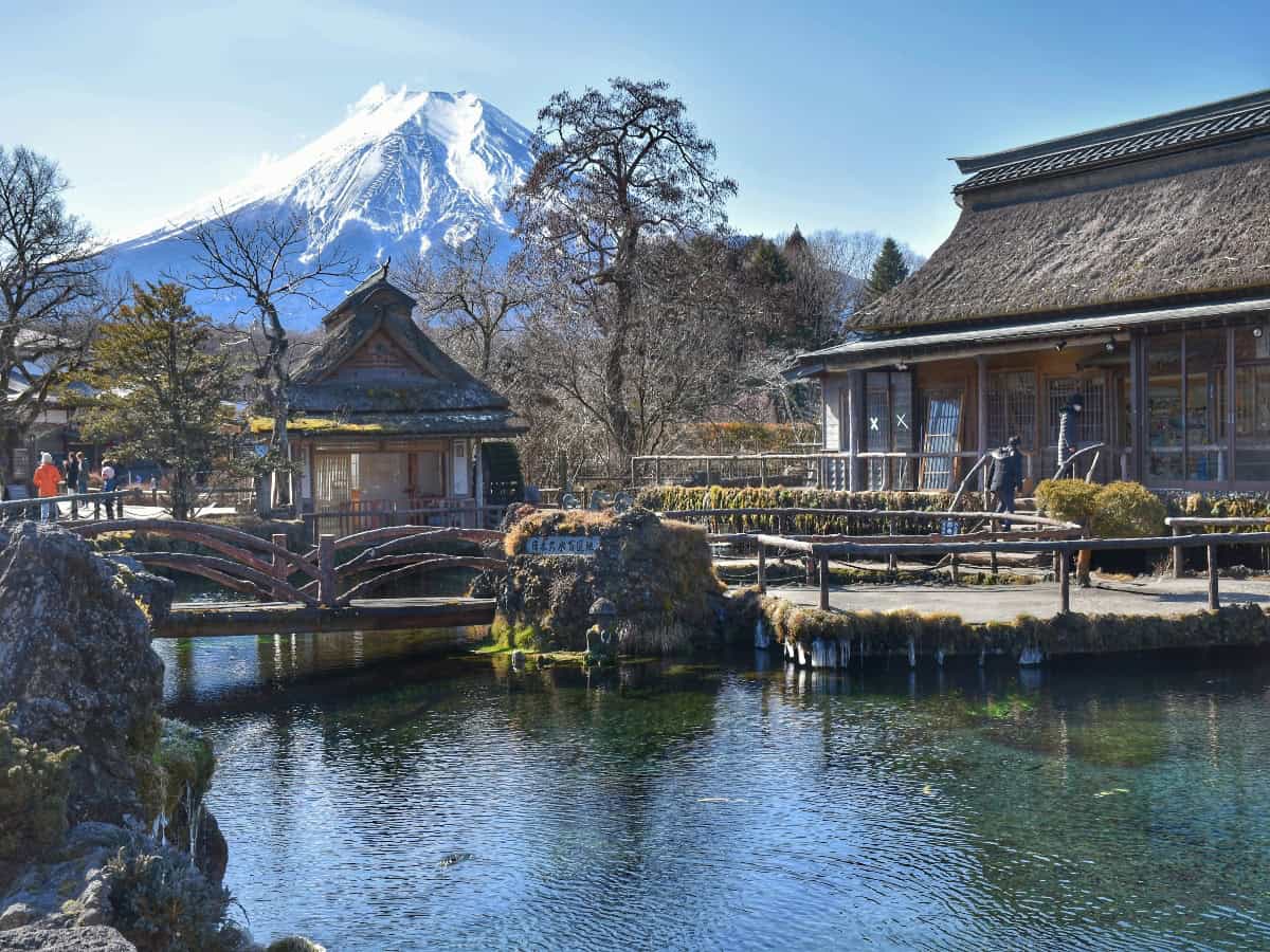cottages arranged around pond in oshino hakkai, with view of mt fuji in background